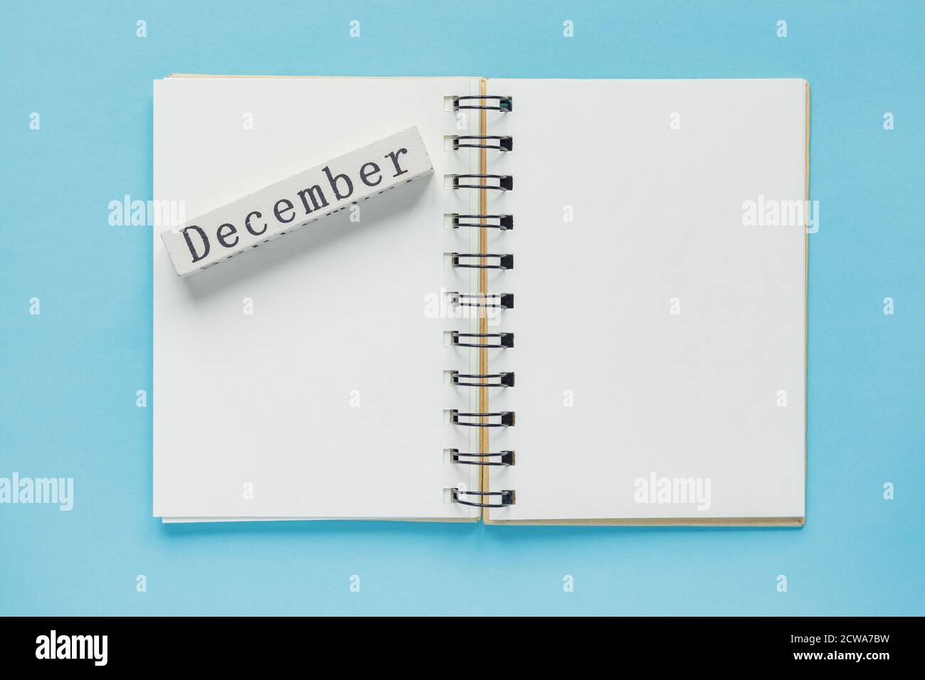 Clean spiral note book for notes and messages and december wooden calendar bar on blue background. Minimal business flat lay Stock Photo