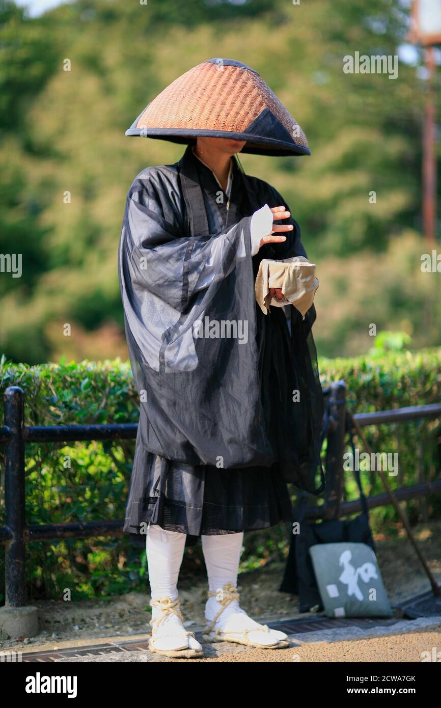 Kyoto, Japan - November 23, 2007: Zen Buddhist monk practices takuhatsu in  traditional robe and straw hat. He exchange chanting of sutras for donatio Stock Photo