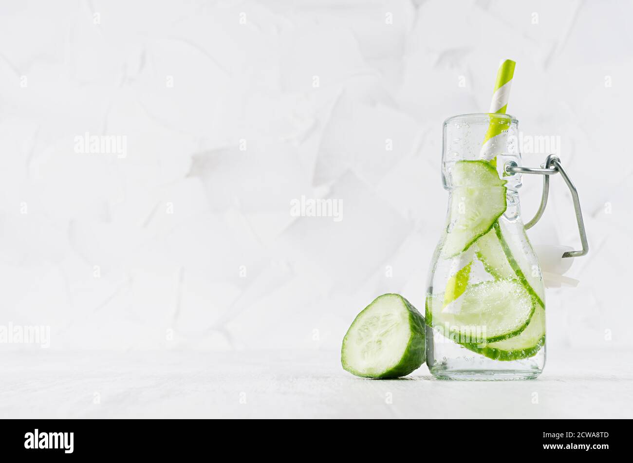 Cold fresh detox beverage of green cucumber with soda water, bubbles, funny striped straw on simple soft bright white background, copy space. Stock Photo