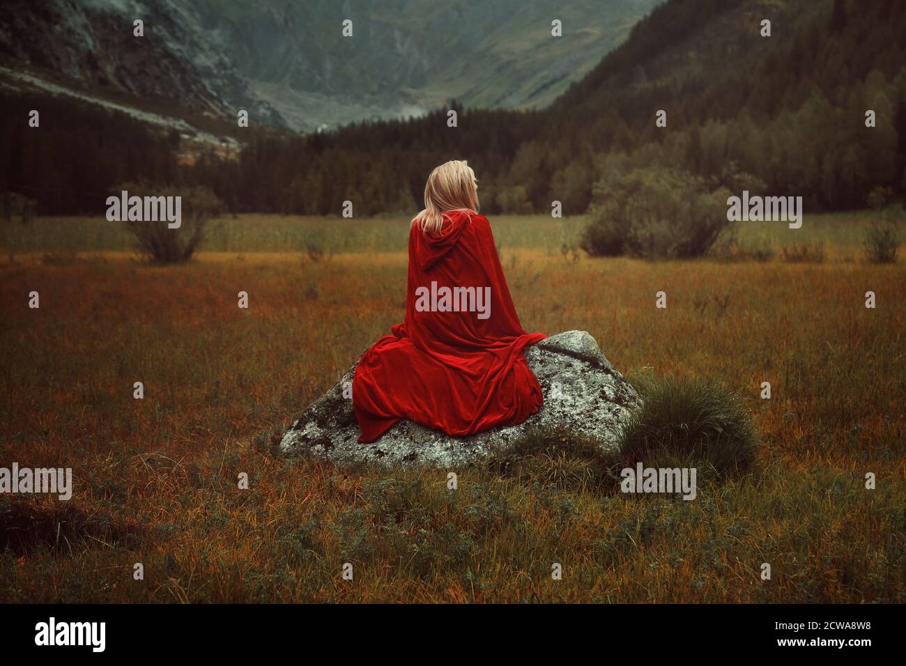 Blond woman with red cloak. Alone on a rock Stock Photo