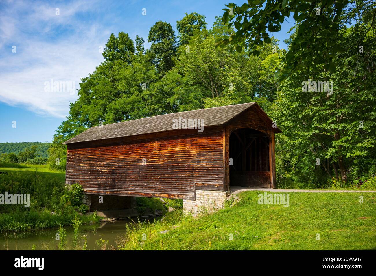 The Hyde Hall Covered Bridge, built in 1825 and is the oldest in the U.S., rests at the end of a dirt road during a summer day. Stock Photo