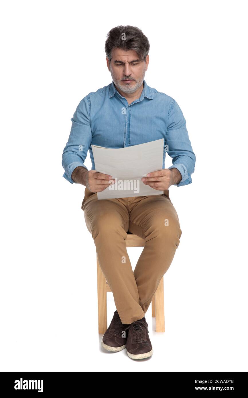 Bothered casual man reading a newspaper and frowning while sitting on a ...