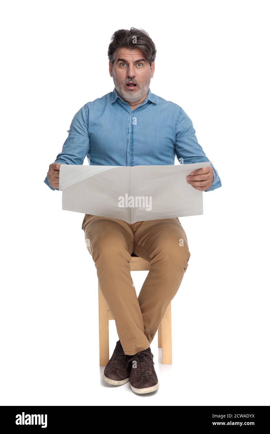 Shocked casual man reading a newspaper and gasping while sitting on a ...