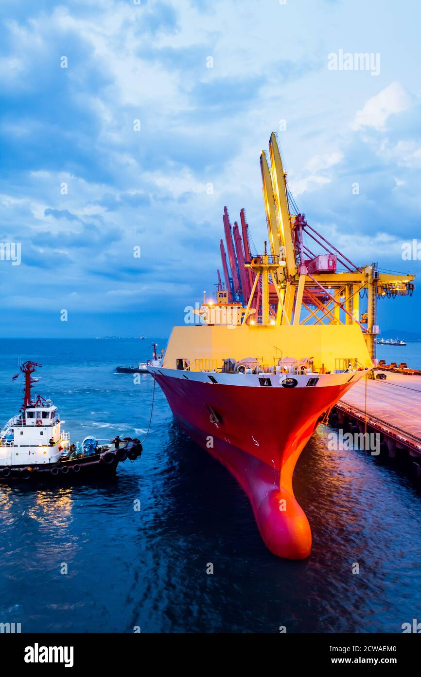 Tugboat push large cargo vessel to berth at port terminal. Port terminal operations and handling equipment. Stock Photo