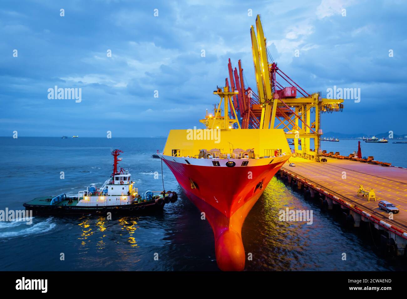 Tugboat push large cargo vessel to berth at port terminal. Port terminal operations and handling equipment. Stock Photo