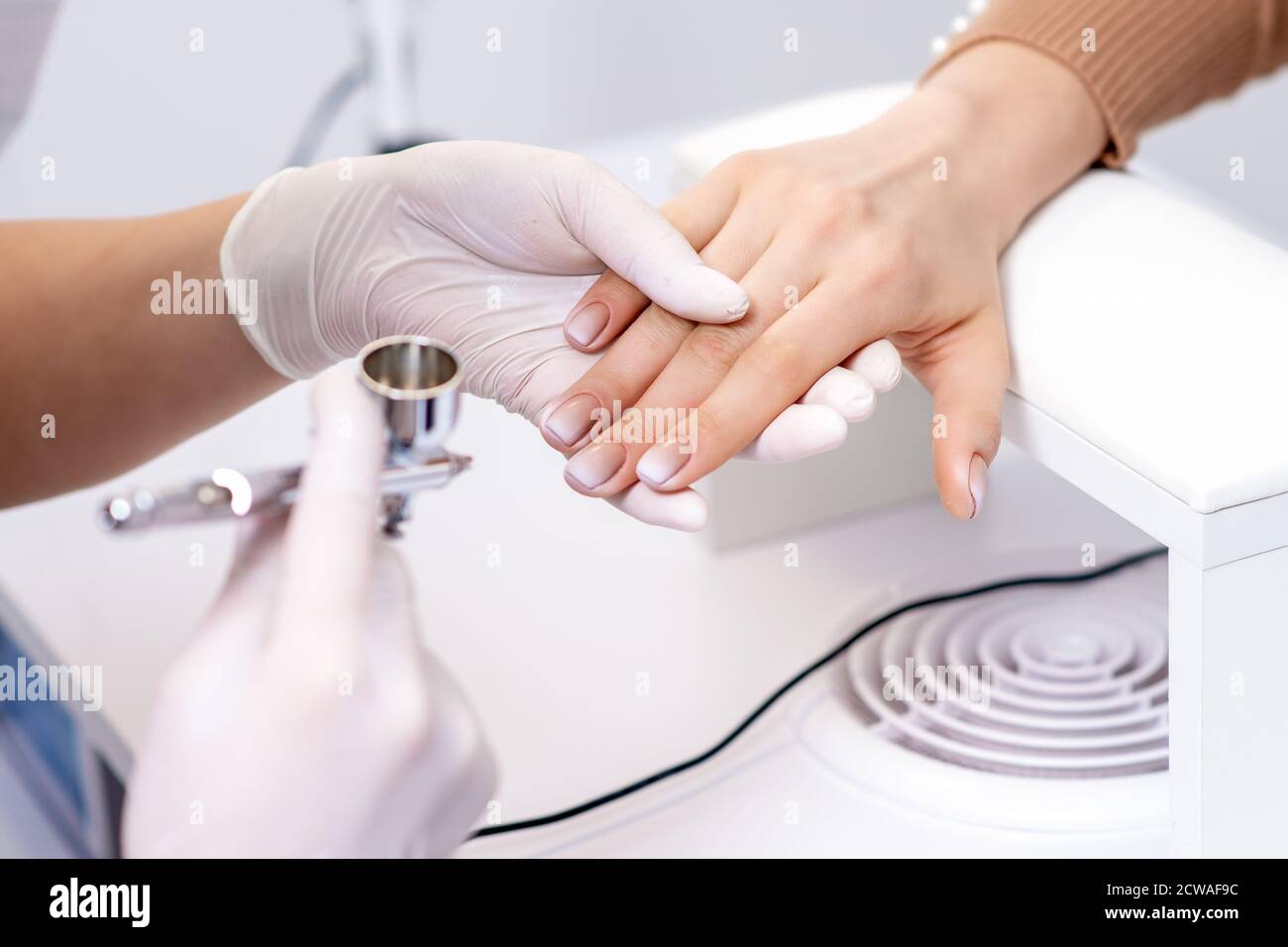 Premium Photo  Young woman receiving manicure by airbrush in nail salon.  procedure for spraying paint on the nails