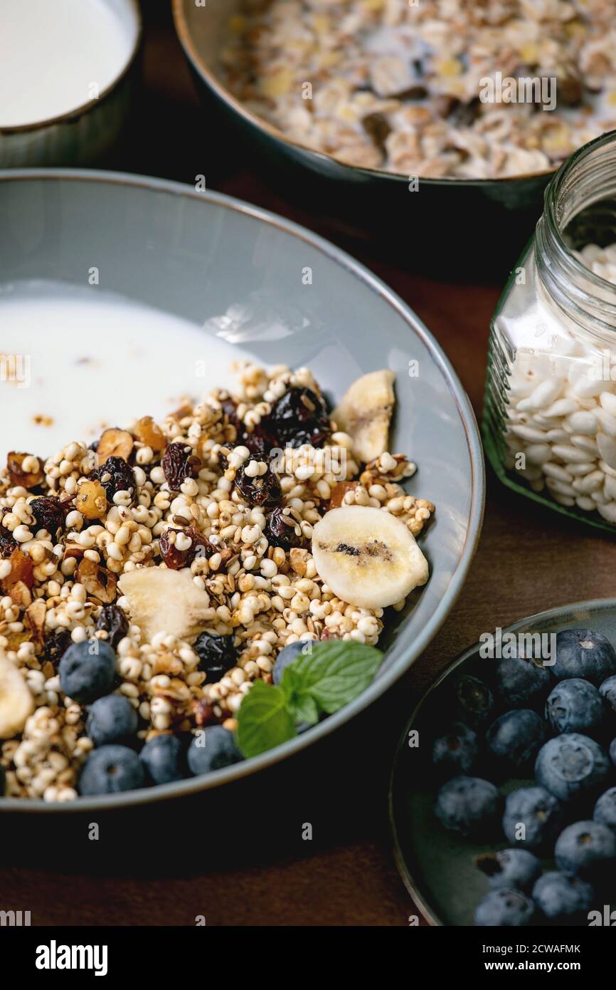 Homemade crunchy puffed millet grain granola with dried fruits and nuts in ceramic bowl, with yogurt, mint and ingredients above. Brown texture backgr Stock Photo