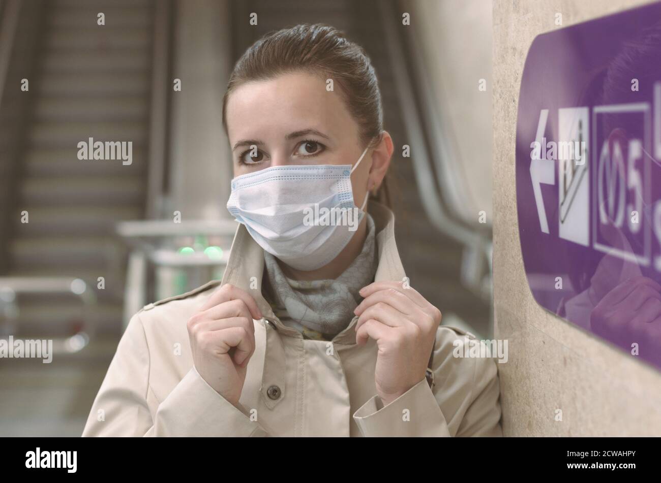 Girl with a medical mask on her face and raised hands in the background of empty escalators and a direction arrow subway Stock Photo