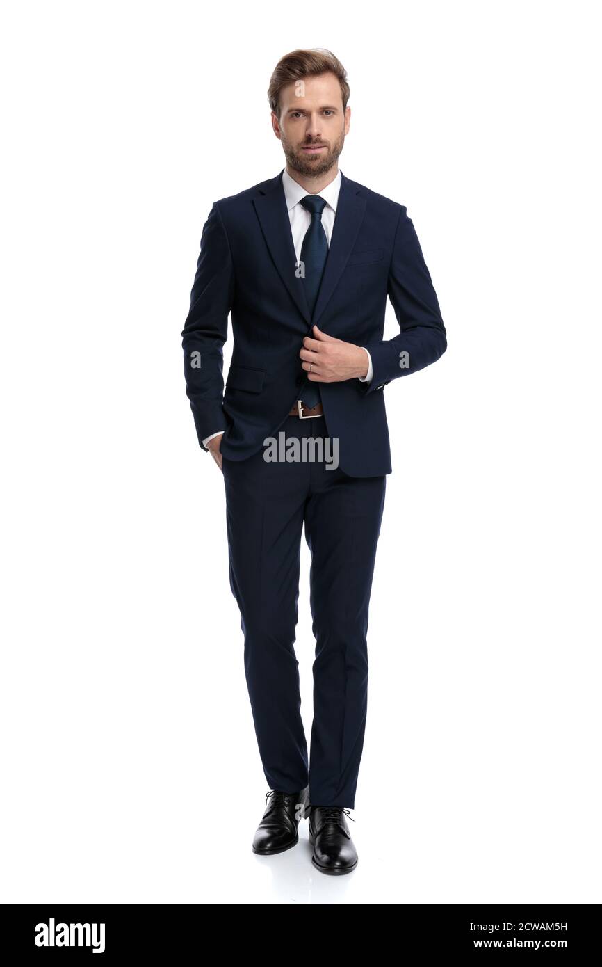 young businessman in navy blue suit adjusting coat and walking isolated