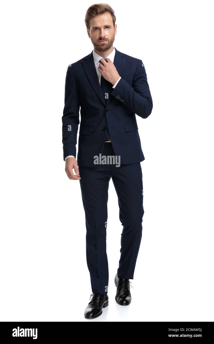 confident businessman in navy blue suit adjusting tie and walking ...