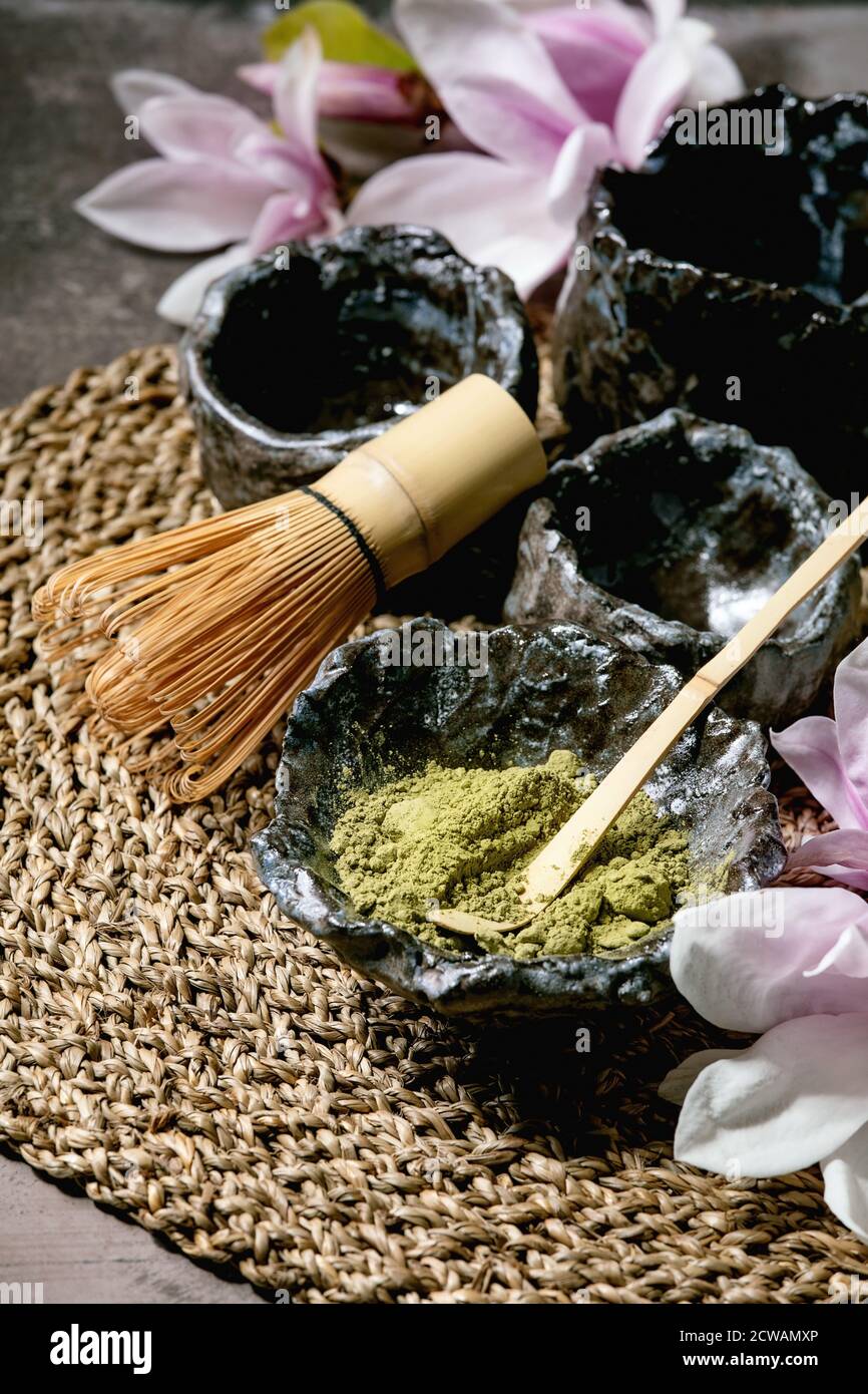 https://c8.alamy.com/comp/2CWAMXP/japanese-matcha-green-tea-powder-in-craft-ceramic-bowl-couple-of-cups-bamboo-whisk-and-pink-magnolia-flowers-on-straw-napkin-over-dark-texture-backg-2CWAMXP.jpg