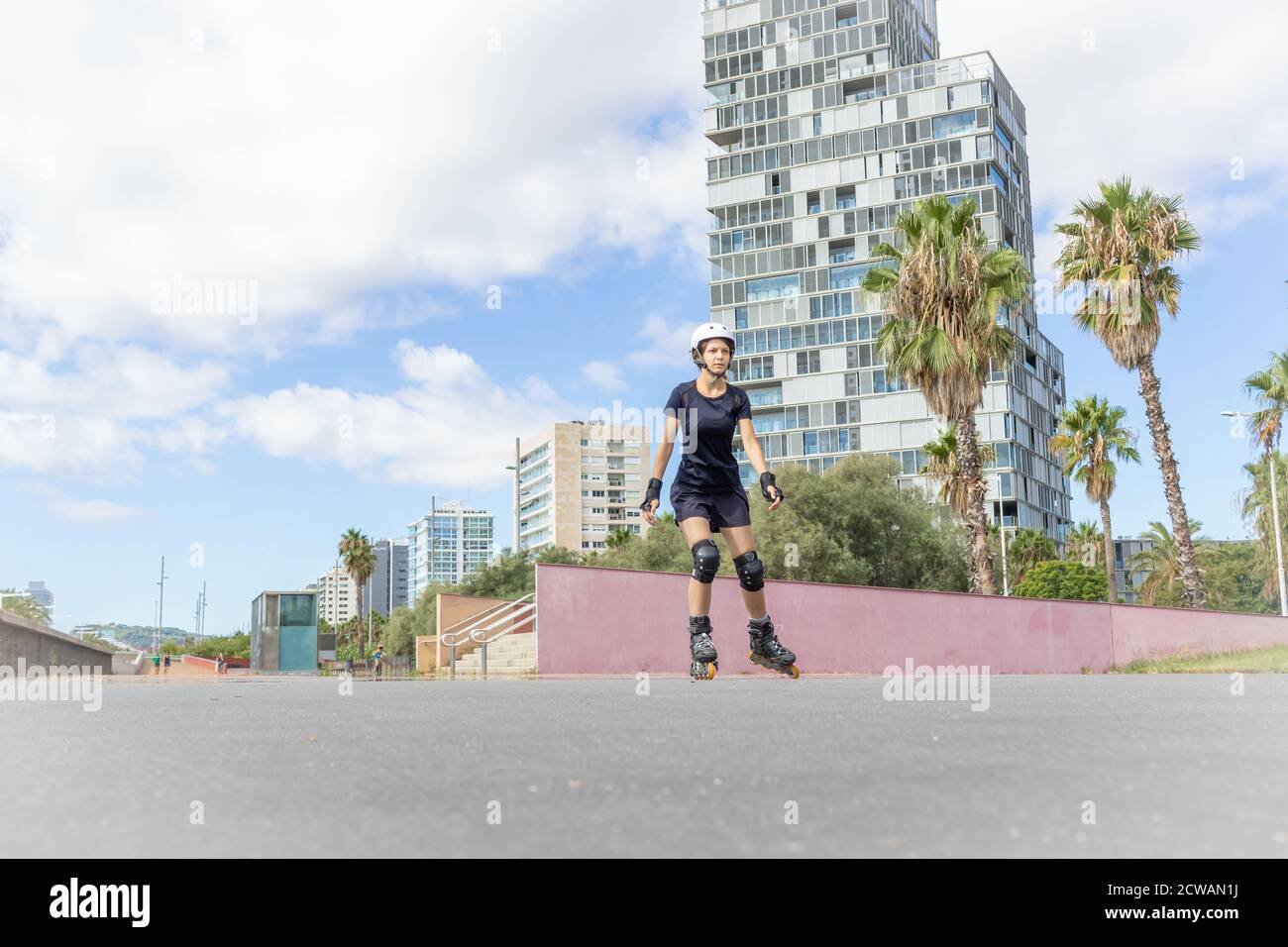 Young roller skater caucasian woman in the white helmet and black sporty clothes, cloudy day, skatepark, urban environment. Stock Photo