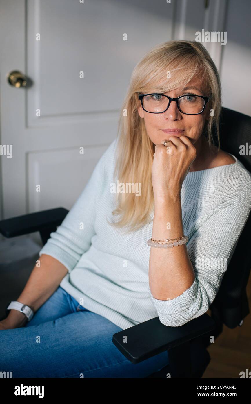 Portrait of smiling mature woman with glasses in her home office ...