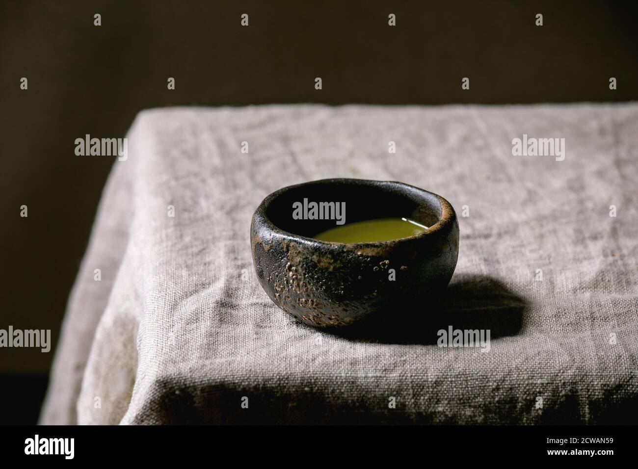 Japanese matcha green tea in wabi sabi ceramic cup with pink magnolia flowers on grey linen table cloth. Stock Photo