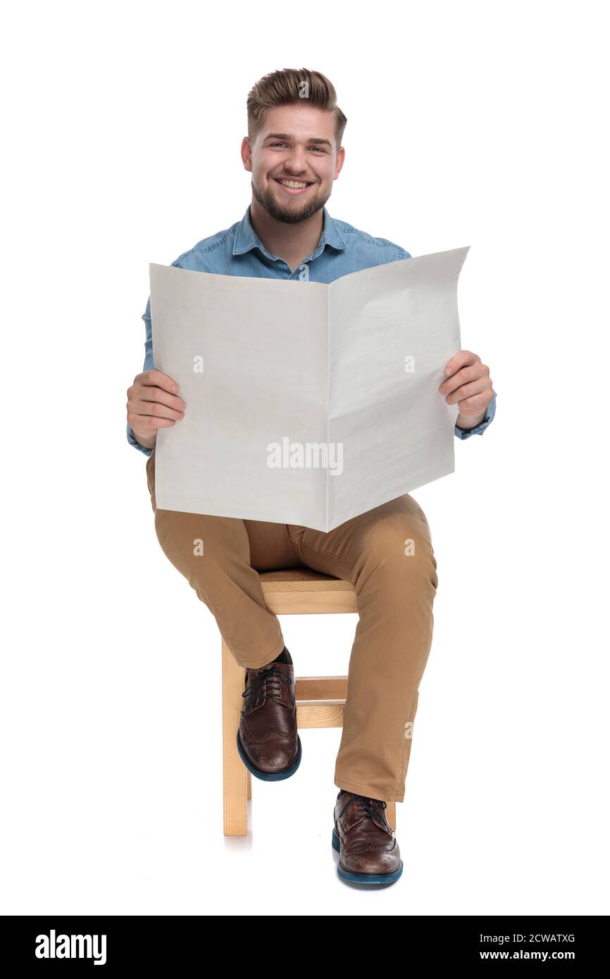 young casual man reading newspaper and smiling, sitting isolated on white background, full body Stock Photo