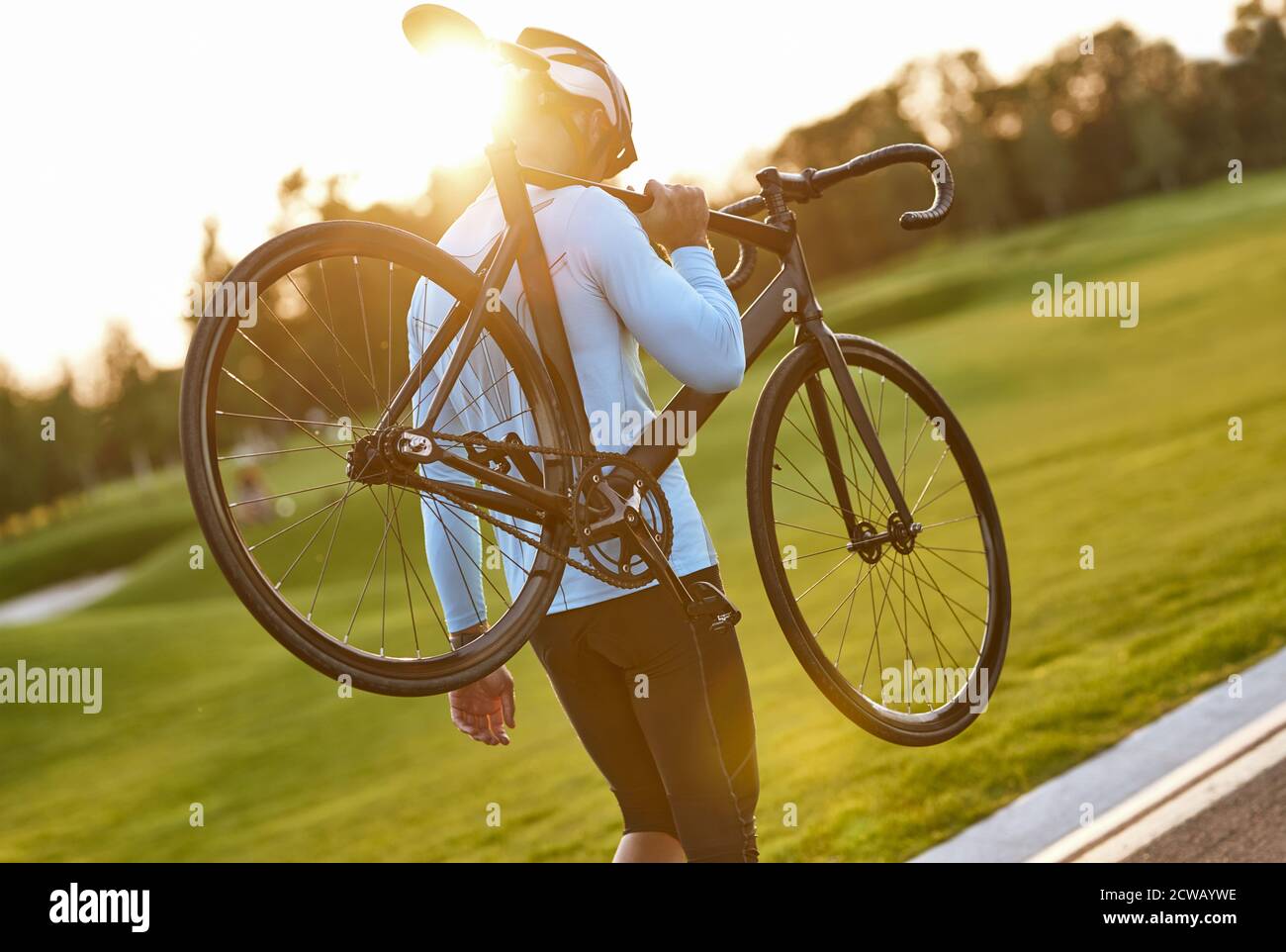 Strong athletic man in sportswear and protective helmet carrying his bicycle after cycling training in park, enjoying amazing sunset. Active lifestyle and sport concept. Biking outdoors Stock Photo