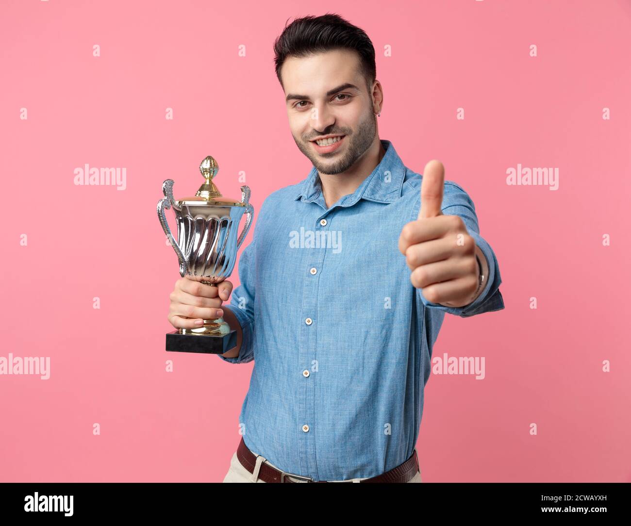 young casual guy holding trophy and making thumbs up sign, standing on ...