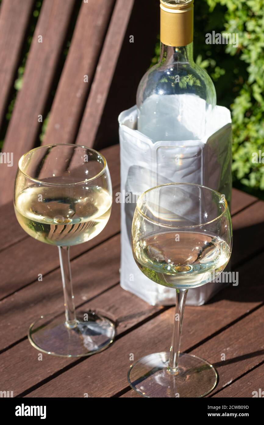 Two wine glasses outside with a bottle of white wine in a cooler sleeve Stock Photo