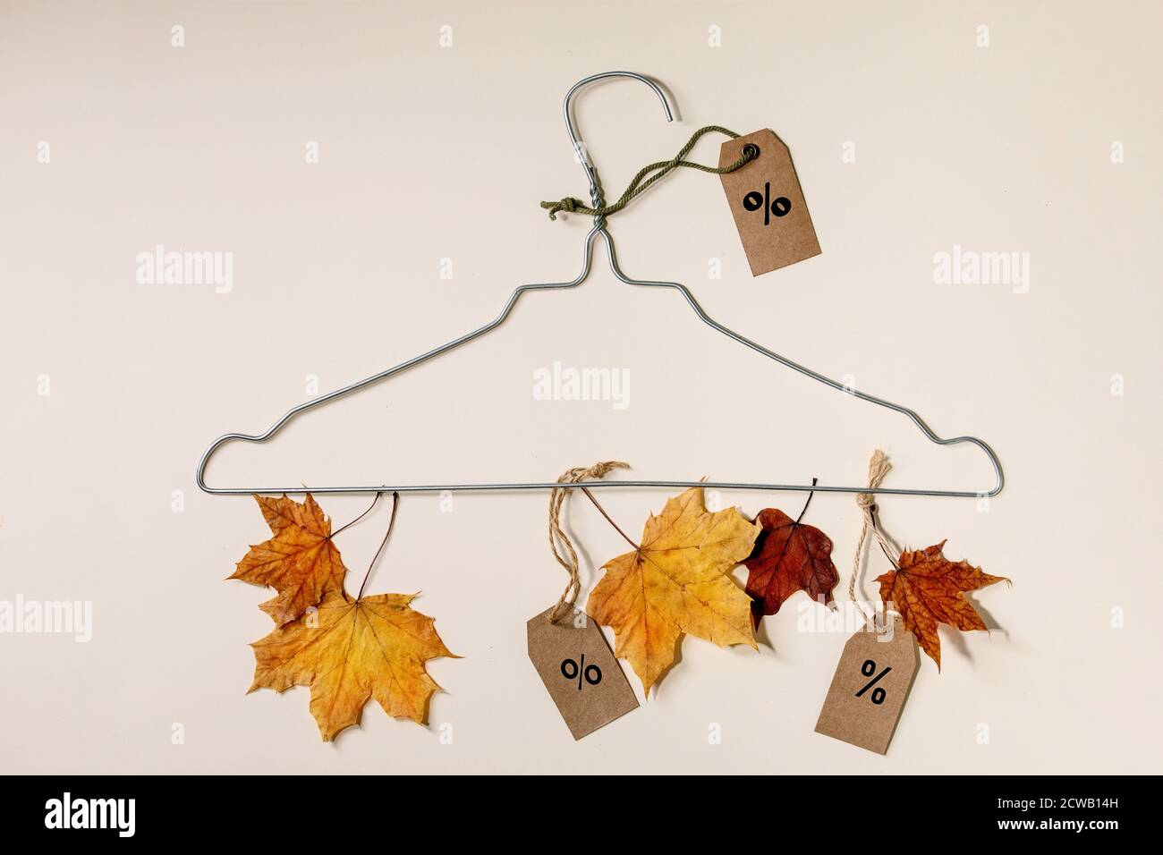 Autumn sale concept. Wire hanger, labels with percents, yellow autumn leaves over beige background. Flat lay. Stock Photo