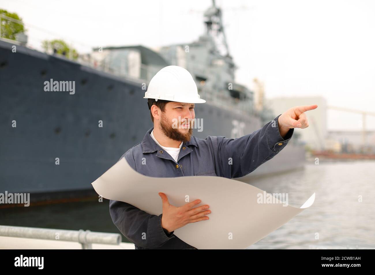 Maritime captain reading blueprints, showing by forefinger and standing near vessel. Stock Photo