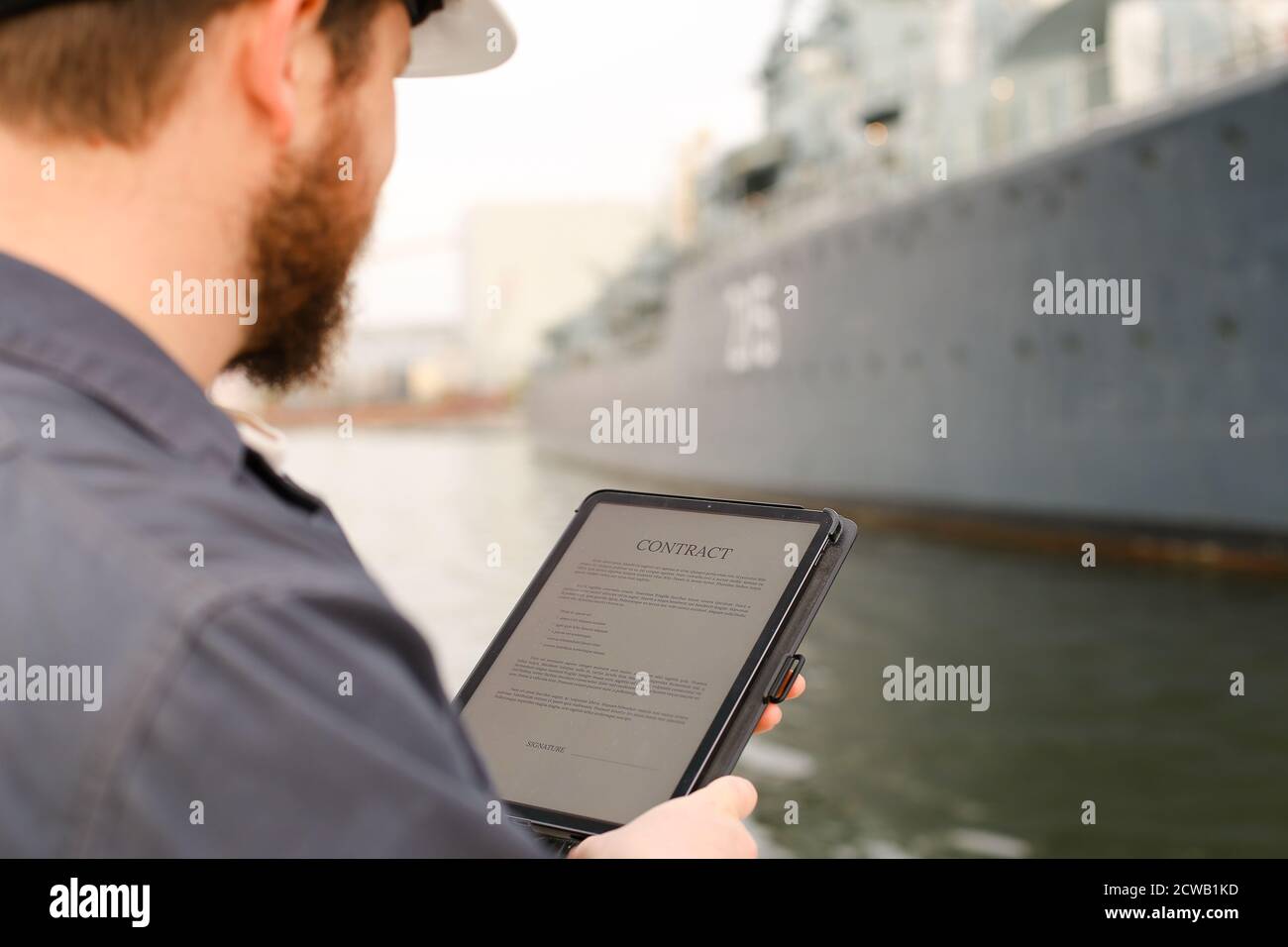 Navigation officer reading contract on tablet near vessel in background. Stock Photo