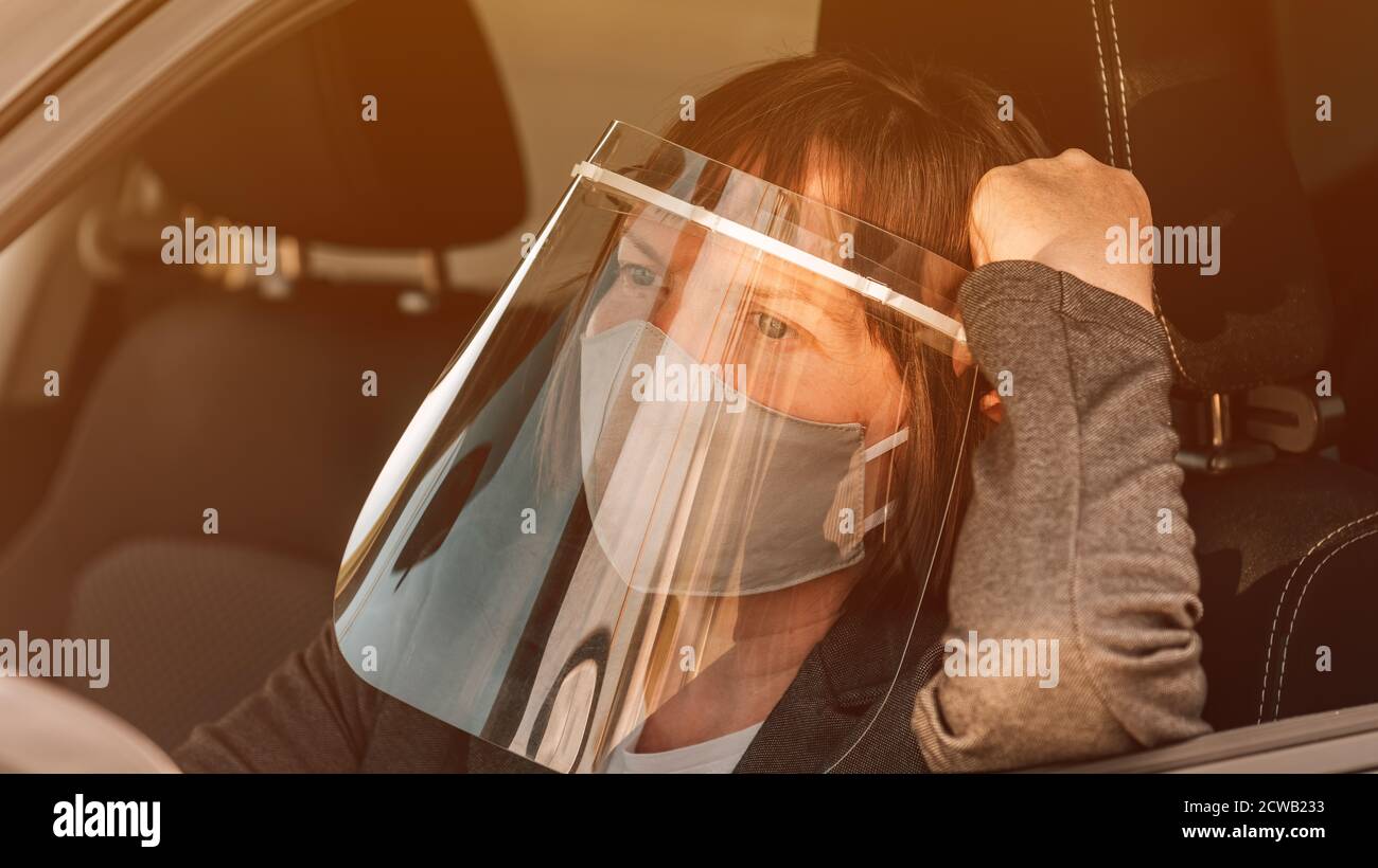 Female taxi driver with protective face mask and plastic visor waiting in car Stock Photo