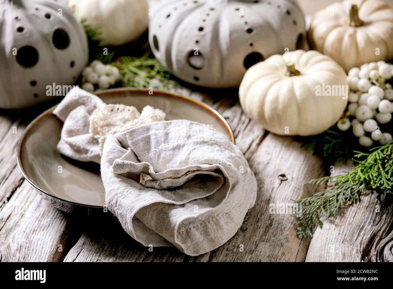 Holiday table setting decoration with white decorative pumpkins, craft clay pumpkins, thuja branches, empty plate with cloth napkin over old wooden ta Stock Photo
