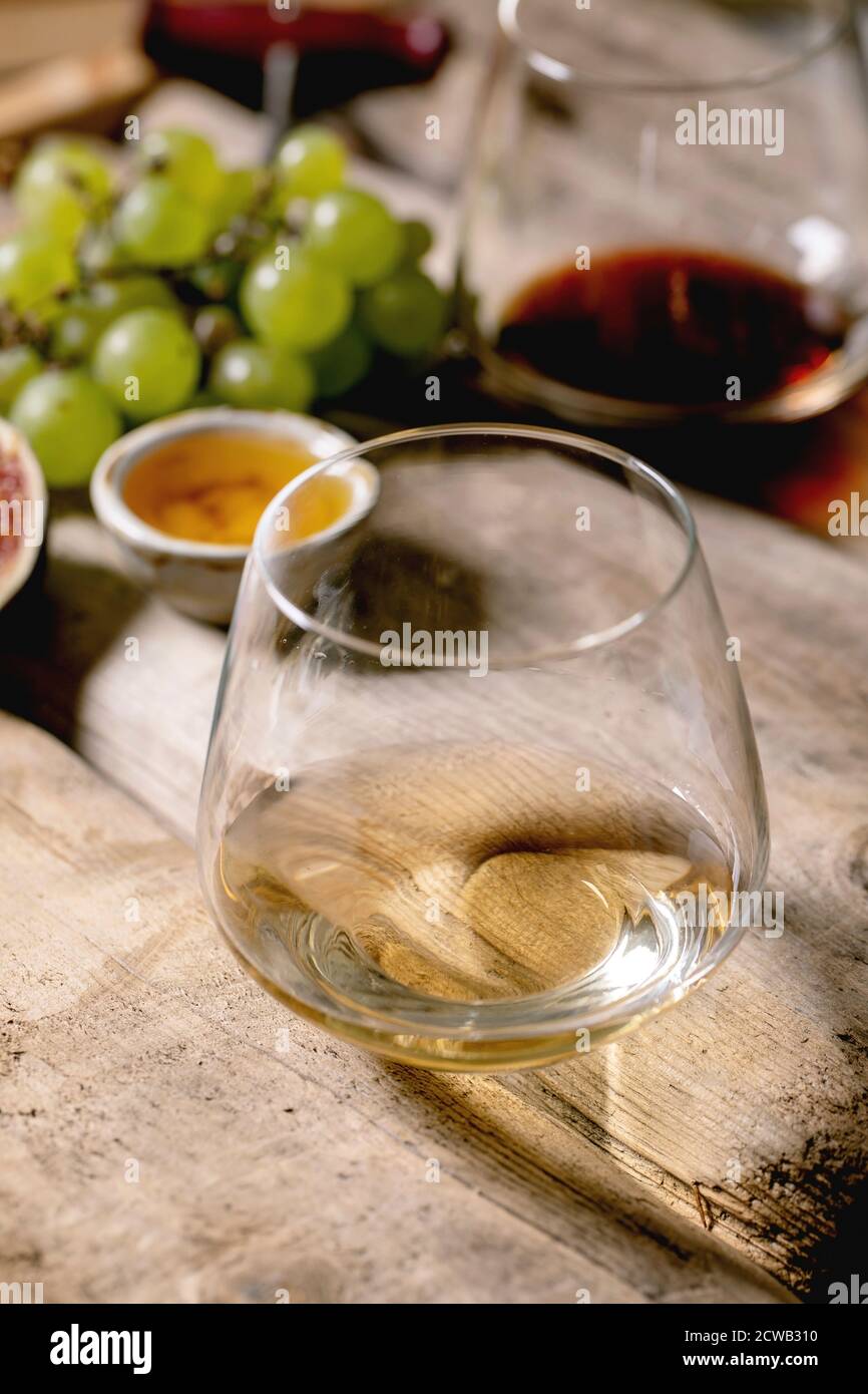 Glasses of red and white wine with grapes, figs, goat cheese and walnuts over old wooden background. Close up Stock Photo