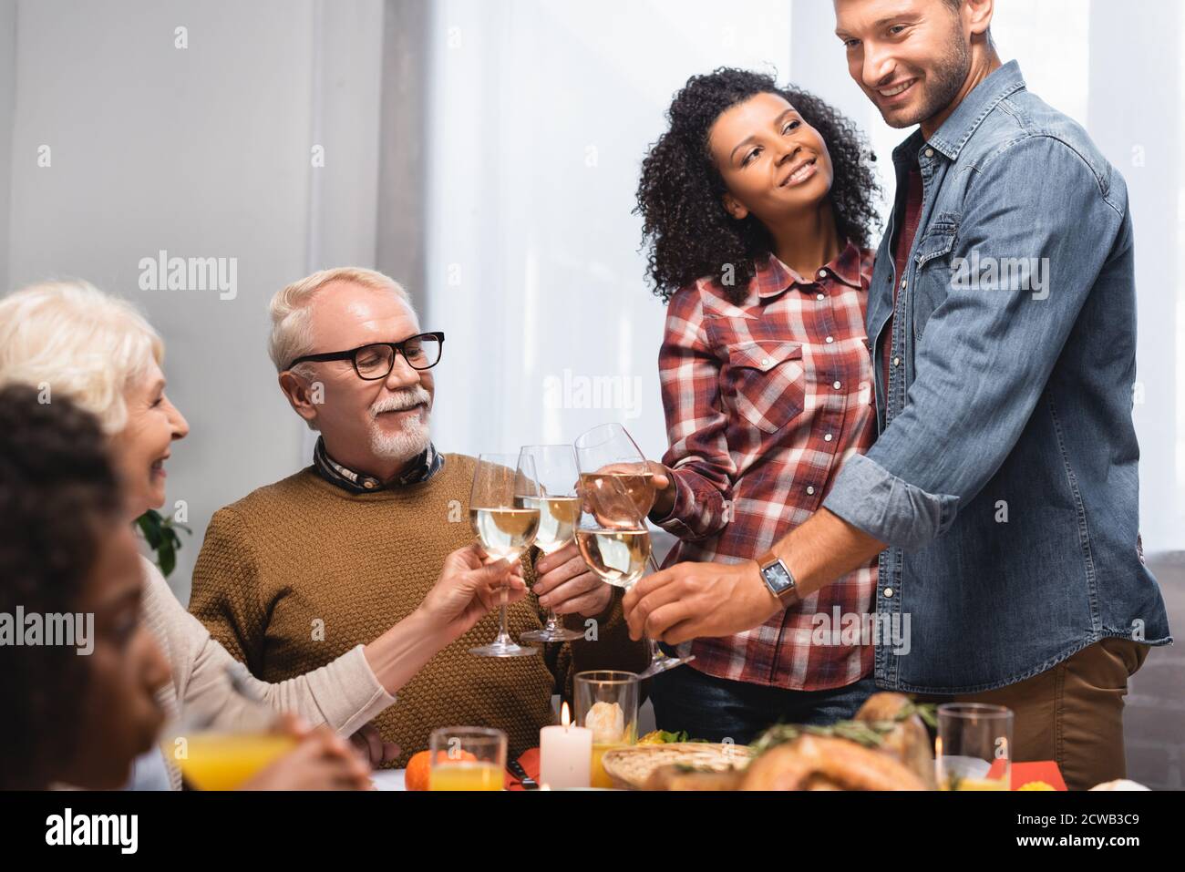 selective focus of multicultural family clinking glasses of white wine while celebrating thanksgiving day Stock Photo