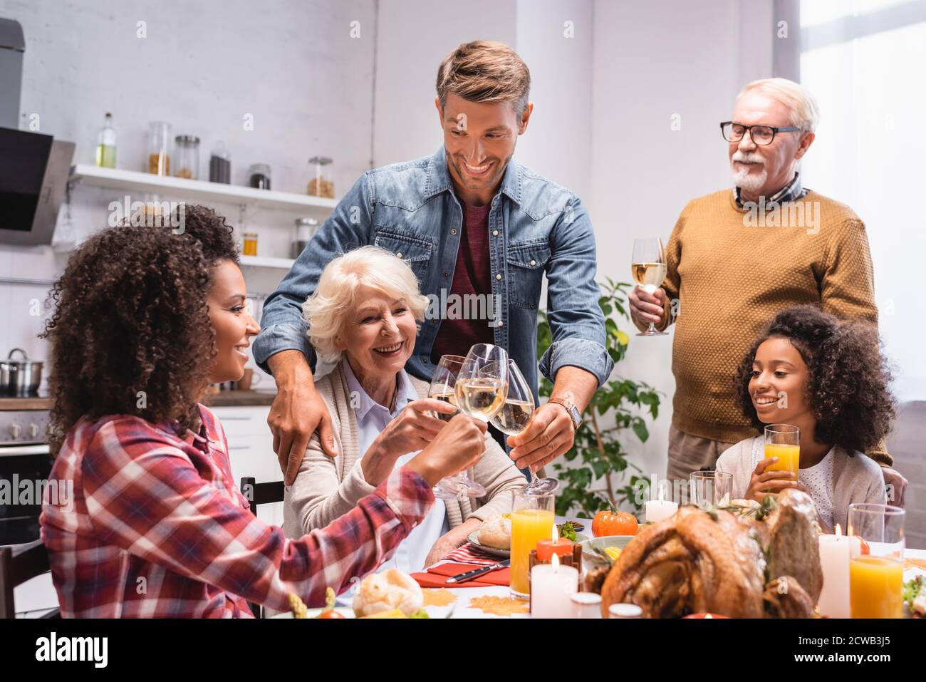 excited multiethnic family clinking wine glasses during thanksgiving dinner Stock Photo