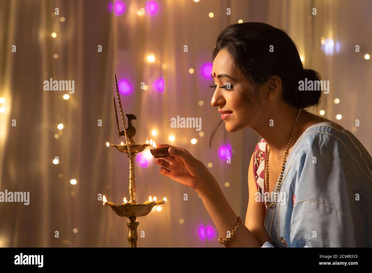 Woman lighting a lamp with diya on the occasion of Diwali Stock Photo