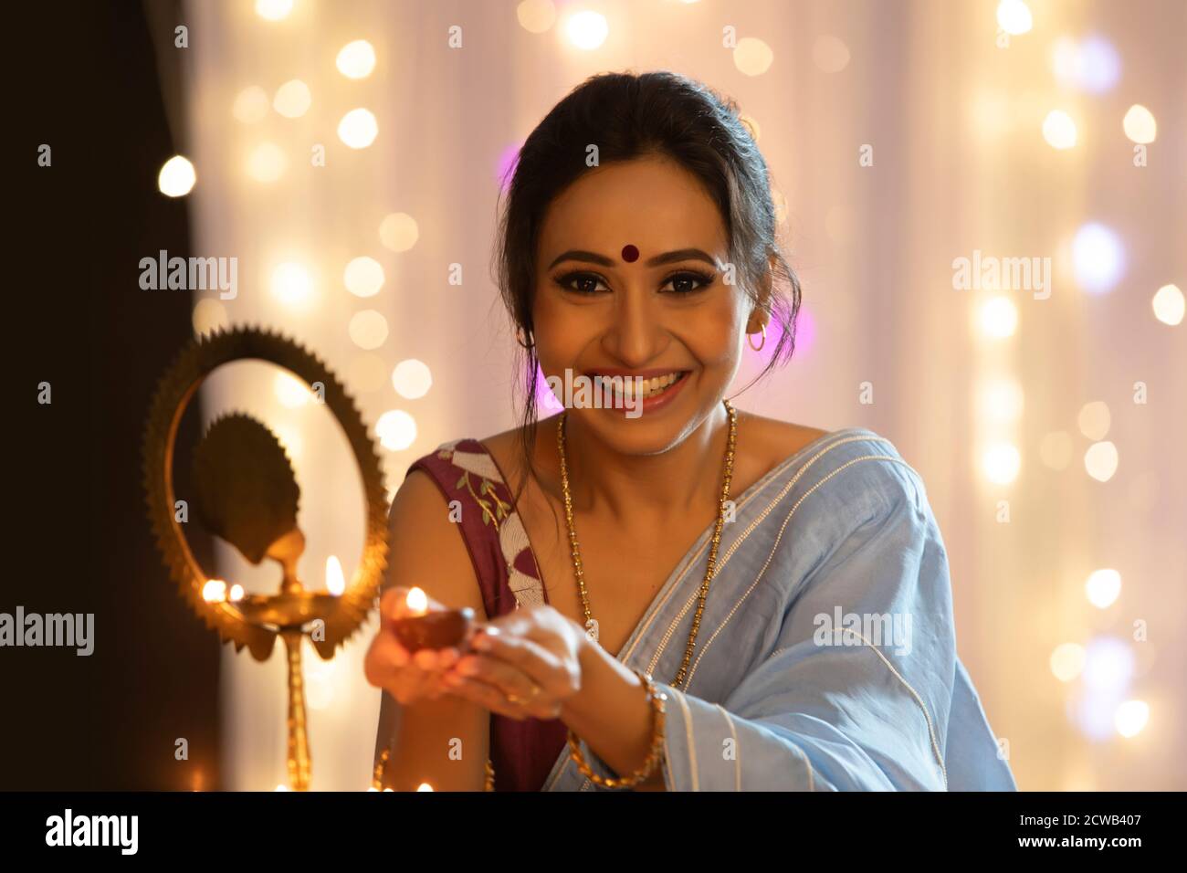 Woman smiling while holding a diya to light a lamp on the occasion of Diwali Stock Photo