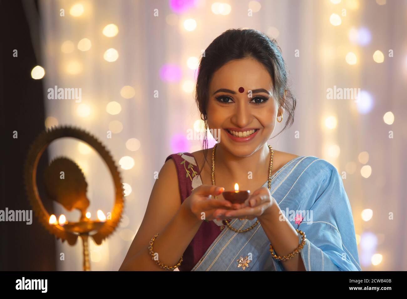 Woman smiling while holding a diya to light a lamp on the occasion of Diwali Stock Photo