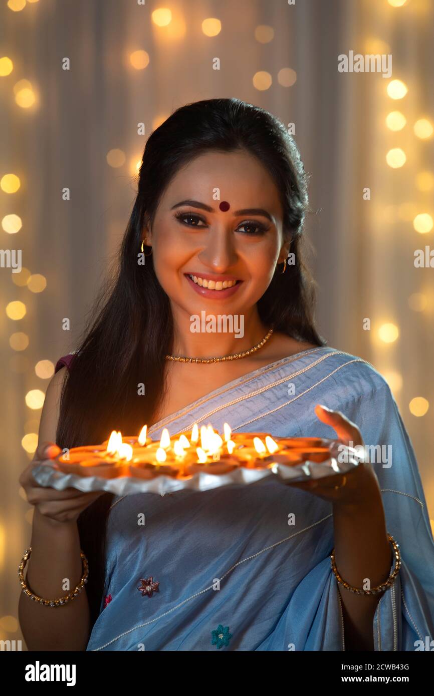 Woman holding a plate full of diyas in her hand and smiling Stock Photo