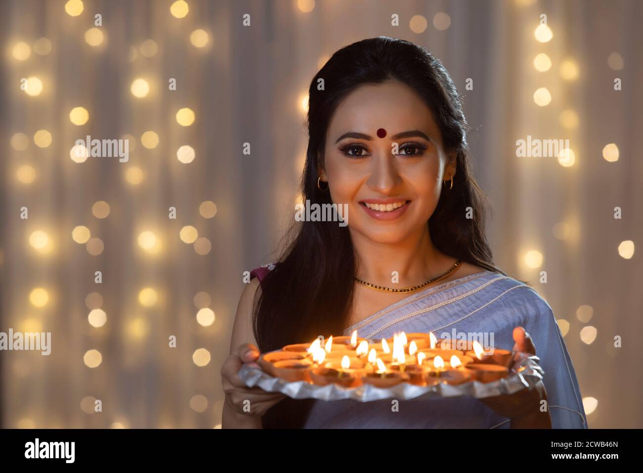 Woman smiling with a plate of diyas in her hand on the occasion of Diwali Stock Photo