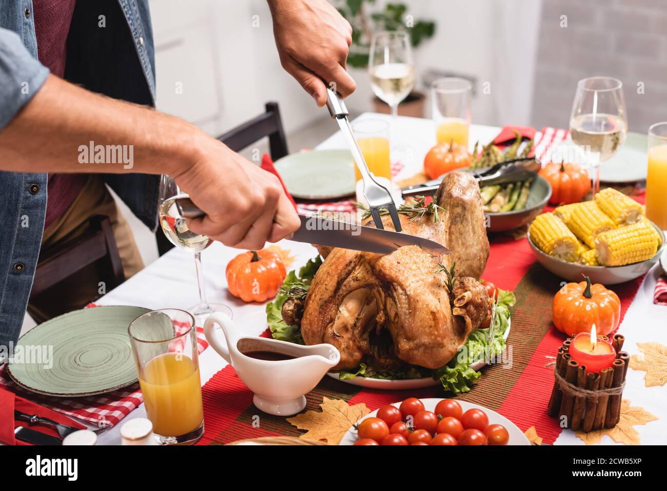 Cropped view of man cutting turkey near thanksgiving decorations on table Stock Photo