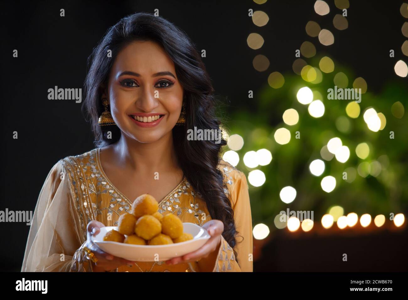 Woman in ethnic attire smiling with a plate full of ladoos in her hand Stock Photo