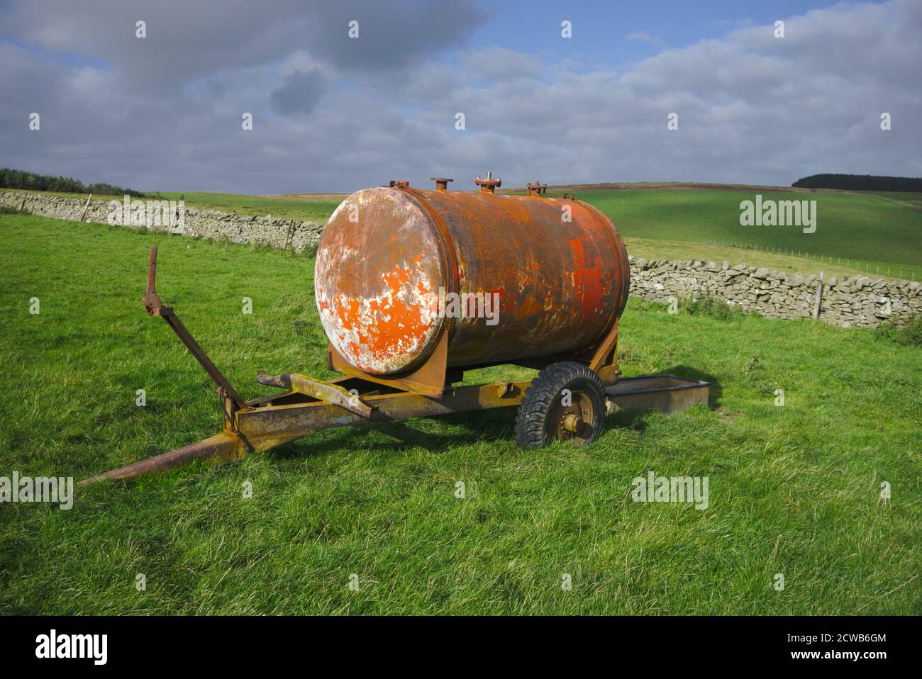 Old cylindrical manure spreader in a field in Berwickshire, Scottish Borders, UK, next to a dry stone wall. Stock Photo