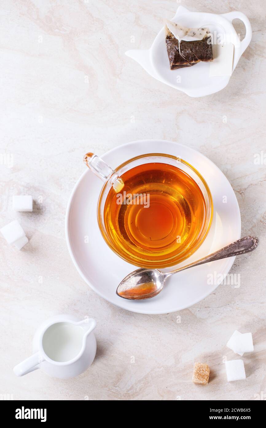 Glass cup of hot tea on saucer with sugar cubes, jug of milk and tea bag  over white marble backgtound. Top view Stock Photo - Alamy, image size:866x1390