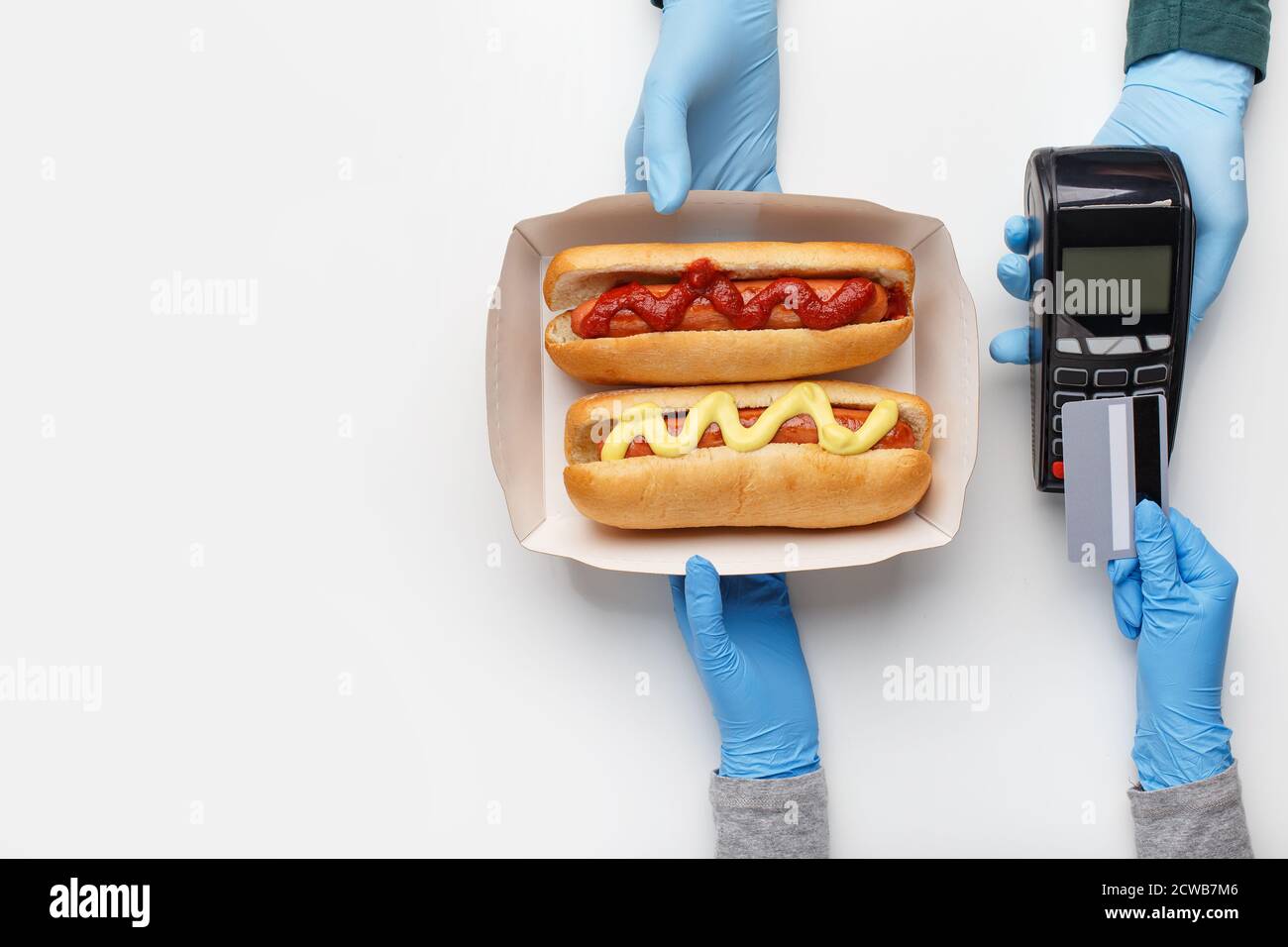 Courier in rubber gloves gives customer cardboard box with hot dogs with grilled sausages, with ketchup and mustard Stock Photo