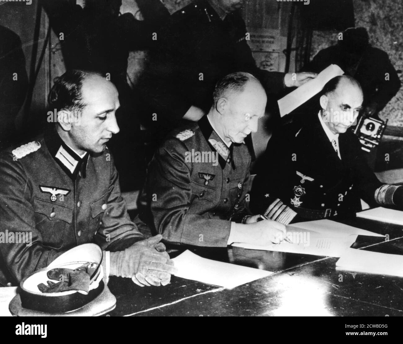 Surrender of Nazi Germany, Reims, France, 7 May 1945. General Alfred Jodl, the German Chief of Staff signing the document confirming Germany's unconditional surrender to the Allies. By his side are his aide Major Wilhelm Oxenius (left) and Admiral Hans Georg von Friedeburg, commander of the German Navy. The photographer is unknown. Stock Photo