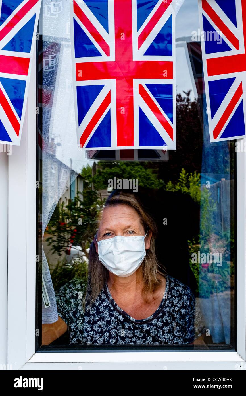 A Woman Looks Out Of Her Window On VE Day During The Corona Virus Pandemic, East Sussex, UK Stock Photo