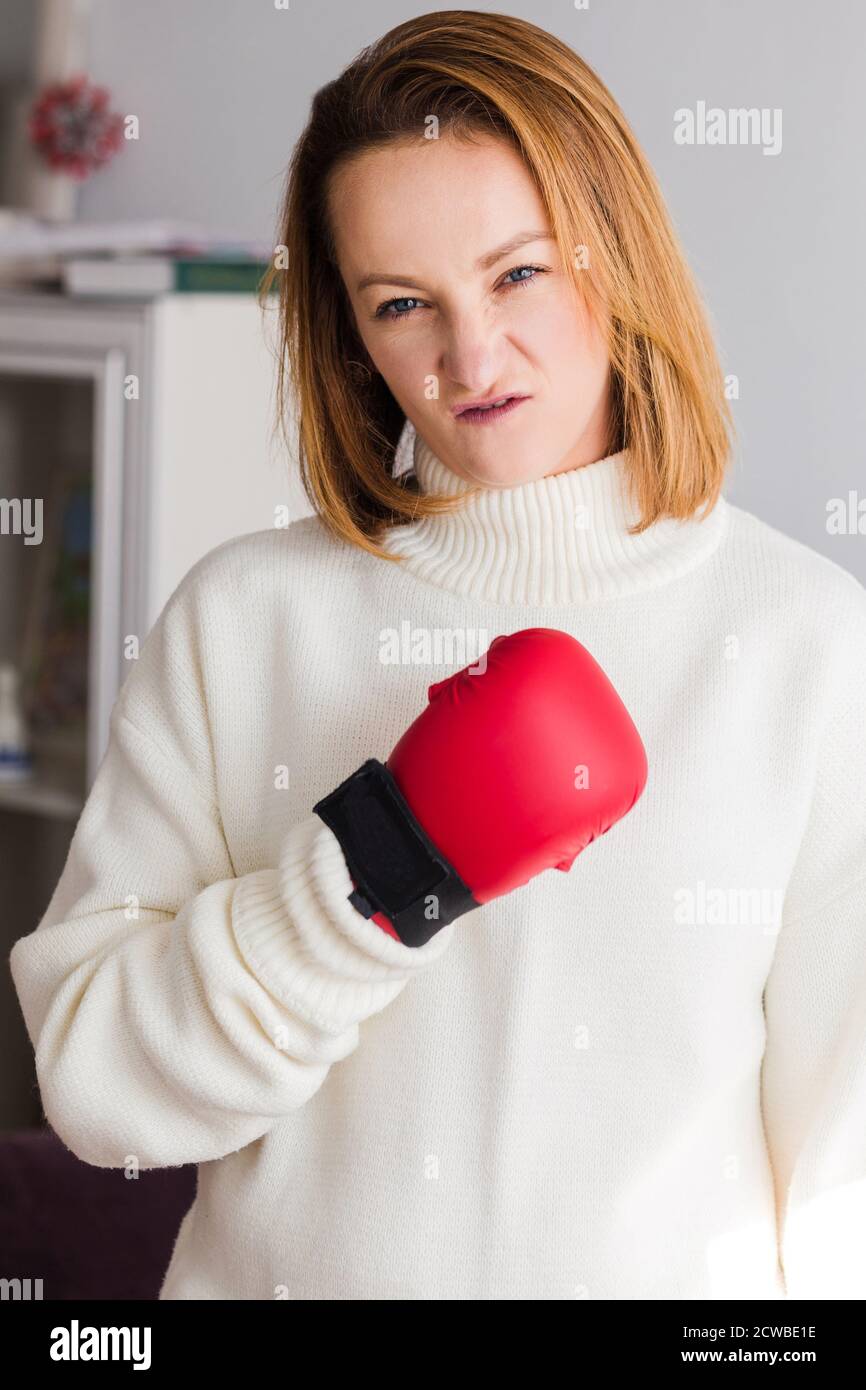 A young woman in a white jacket and a red boxing glove looks into the camera. Concept of struggle, perseverance and achievement of goals Stock Photo