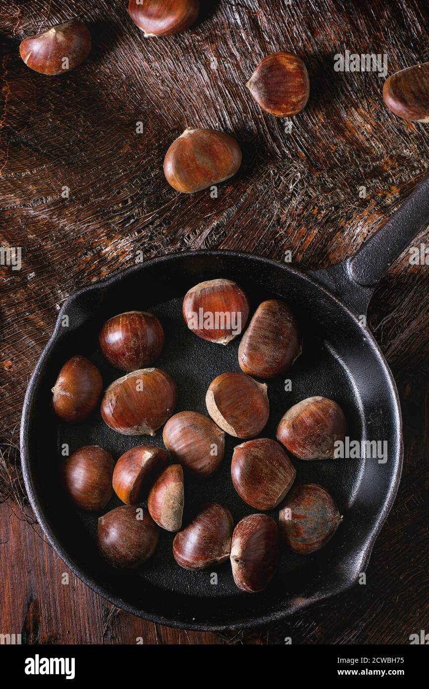 Uncooked edible chestnuts in cast iron skillet over wooden table. Top view Stock Photo