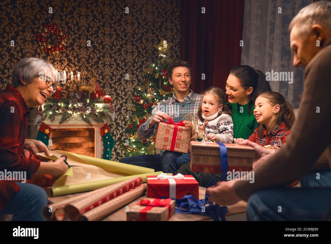 Merry Christmas and Happy New Year! Grandma, grandpa,  mum, dad and daughters near the tree at home. Family preparing for Holiday. Stock Photo