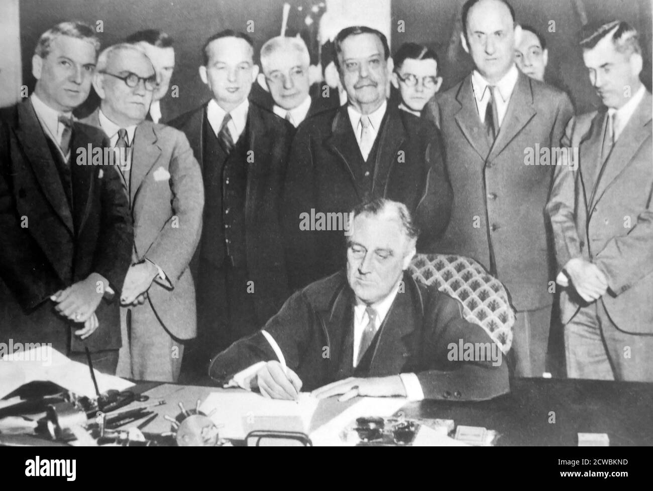 Black and white photo of US President Franklin D. Roosevelt (1882-1945) in the White House signing a document surrounded by his principal collaborators from Brain Trust, a name given to the president's closest advisors. Stock Photo