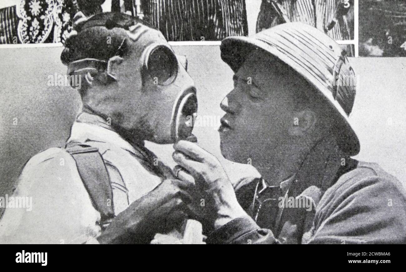 Black and white photo of the War in Ethiopia after the Italian invasion of 1935; a European instructor teaching an Ethiopian soldier how to put on a gas mask. Stock Photo