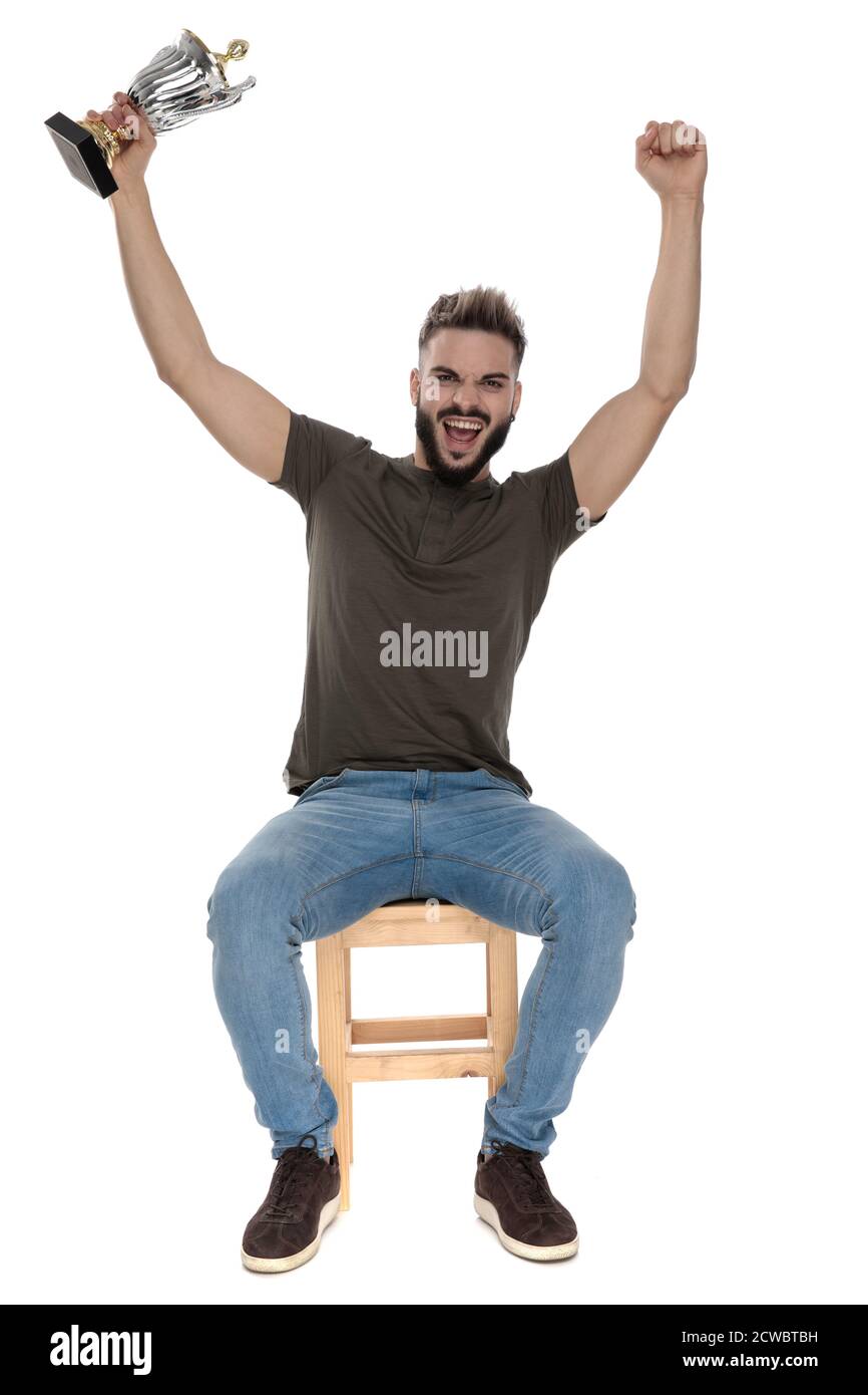 Celebrating casual man holding a trophy and yelling while sitting on a ...