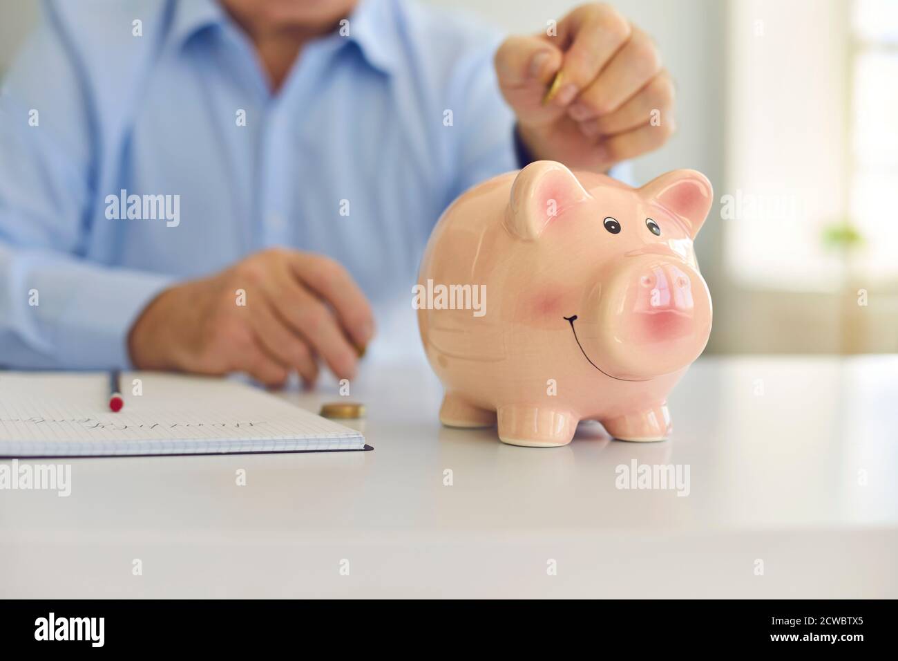 Senior man saving money and putting coin in cute shiny piggy bank ...