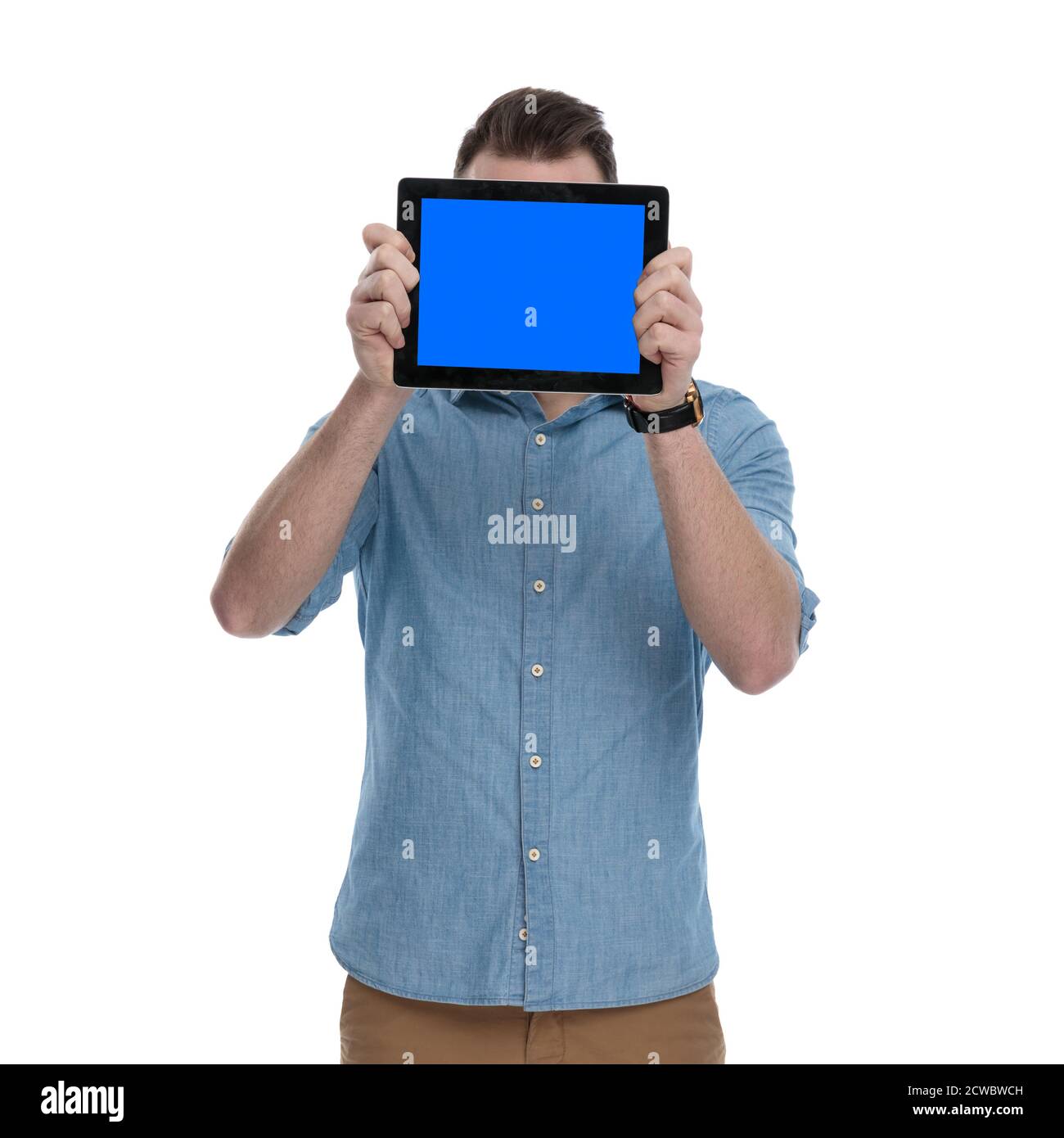 Young casual man covering his face with empty tablet while wearing blue ...